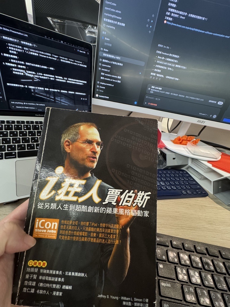 BLAKE 手持《i狂人賈伯斯》舊書，背景是正在工作的電腦螢幕
